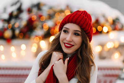 A beautiful  woman with red lips in a warm hat stands by a decorated christmas van on the street