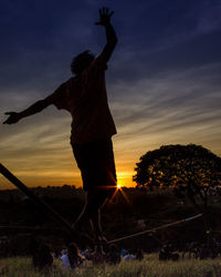Silhouette man doing stunt on field against sky during sunset