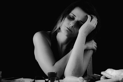 Close-up of depressed woman sitting at desk against black background