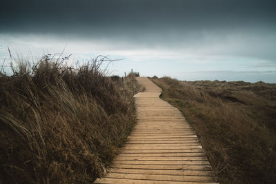 Boardwalk leading towards landscape against sky