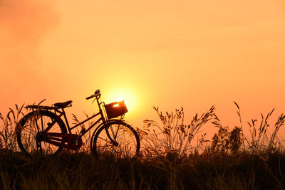 Silhouette bicycle parked on grassy field against sky during sunset