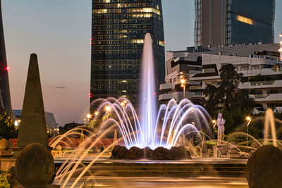 Illuminated fountain against buildings at night