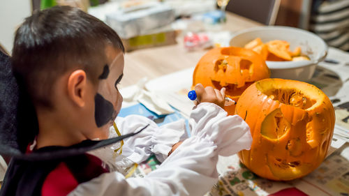 High angle view of cute boy drawing on pumpkins at home during halloween