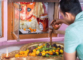 Man offering holy water to hindu god shivalinga worshiped with flower and bell paper at temple