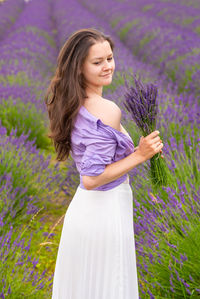 Beautiful woman standing by purple flower on field