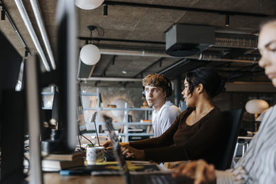 Male and female computer programmers discussing while sitting at desk in office