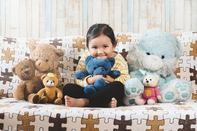 Portrait of girl sitting with teddy bears on sofa at home