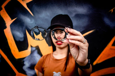 Portrait of young woman holding eyeglasses while standing outdoors