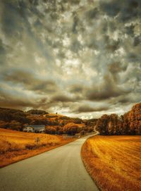 Road passing through field against cloudy sky