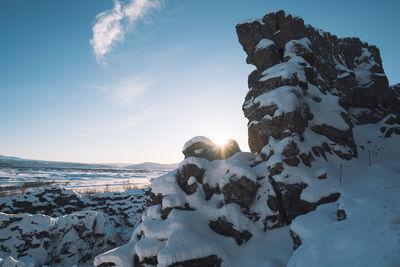 Frozen rocks on shore against sky during winter