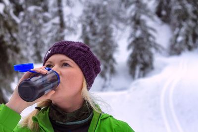 Close-up of young woman drinking water on snowy field