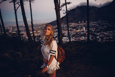 Portrait of young woman standing on field against sky during sunset