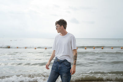 Full length of young man standing at beach against sky