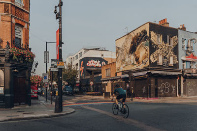 Woman riding bicycle on street against buildings in city