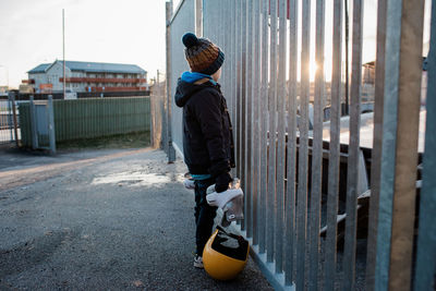 Young boy holding his ice skates looking out at an ice rink