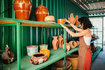 Side view of cheerful female potter standing by display in pottery shop