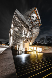 Illuminated ferris wheel by bridge against sky at night