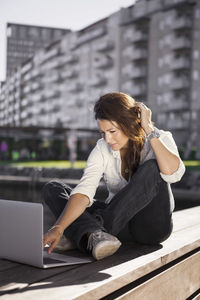 Businesswoman using laptop while sitting on boardwalk