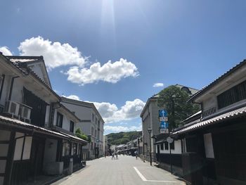 Road amidst buildings against sky on sunny day