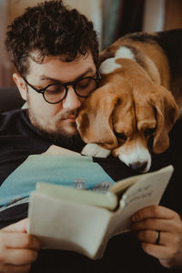 Man reading book while sitting with dog at home