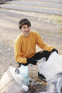 Portrait of smiling male volunteer with plastic waste kneeling on ground