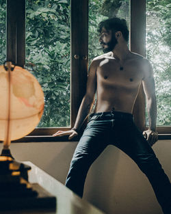 Rear view of shirtless man looking through window