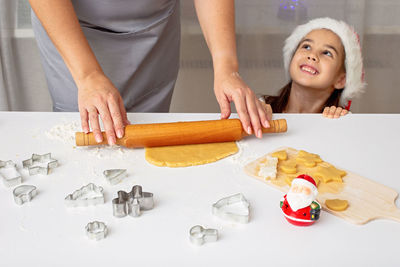 Woman's hands in a  apron, roll out the dough for christmas cookies with a rolling pin on a table.