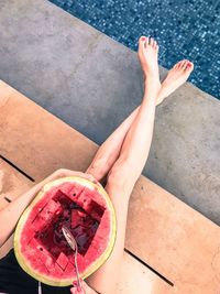 Low section of woman having watermelon while sitting at poolside