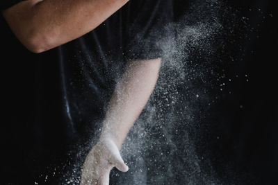 Close-up of hand holding ice cream over black background