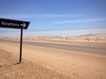 Road sign by highway at skeleton coast against sky