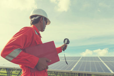 Low angle view of male technician holding equipment against solar panels