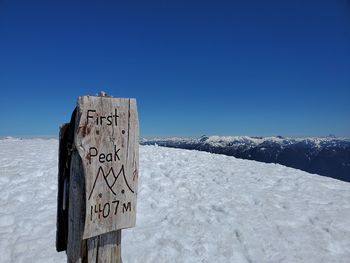 Mountain peak sign with text on snow covered landscape against blue sky