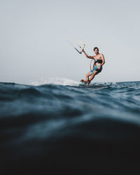 Side view of man kiteboarding in sea against clear sky