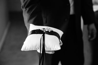 Midsection of bridegroom holding wedding rings on cushion