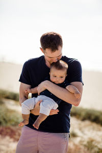 Father holds & kisses son while standing on beach