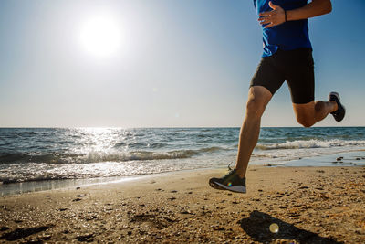 Low section of man running on beach against sky