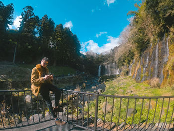 Man sitting on railing against trees