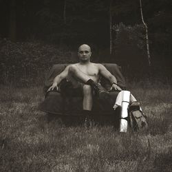 Portrait of shirtless man sitting on armchair at field in forest