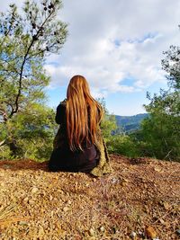 Rear view of woman sitting on rock against sky