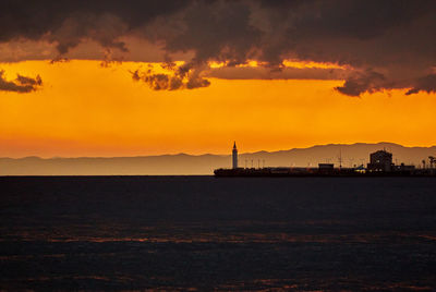 Silhouette pier by sea against orange sky