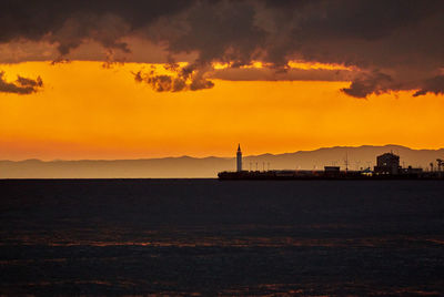 Silhouette pier by sea against orange sky