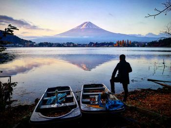 Rear view of man by boats at lakeshore against sky