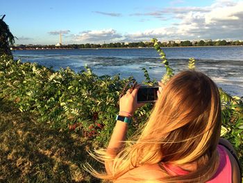 Rear view of woman photographing sea against sky