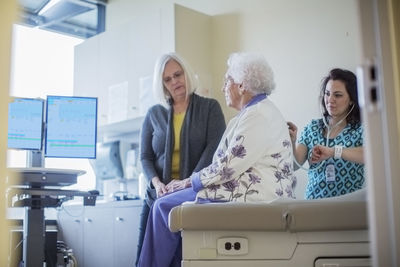 Daughter looking at female doctor listening mother's breathing in hospital ward