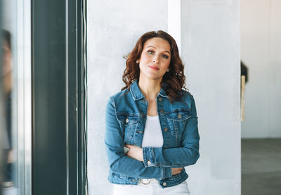 Portrait of smiling charming young woman in jeans jacket near window in the modern building