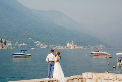 People standing on sea by mountain against sky