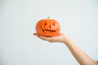 Close-up of hand holding pumpkin against white background