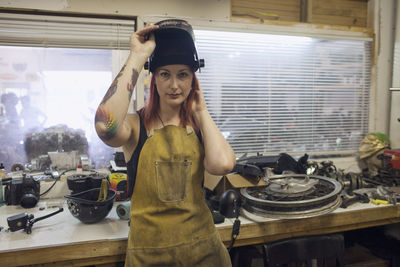 A young woman in a dirty apron and welding mask.