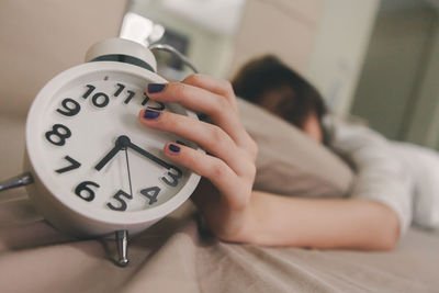 Woman holding alarm clock while sleeping on bed at home