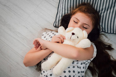 High angle view of girl with stuffed toy sleeping on floorboard at home